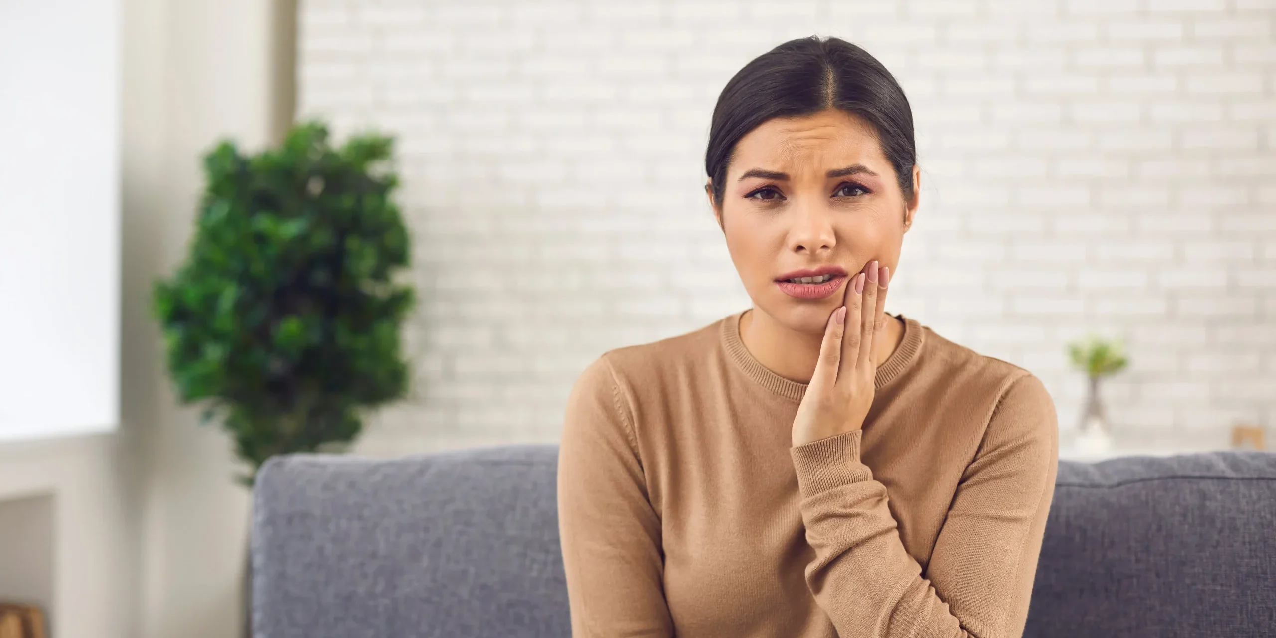 A woman seated on a couch holding her hand to her cheek wincing in pain