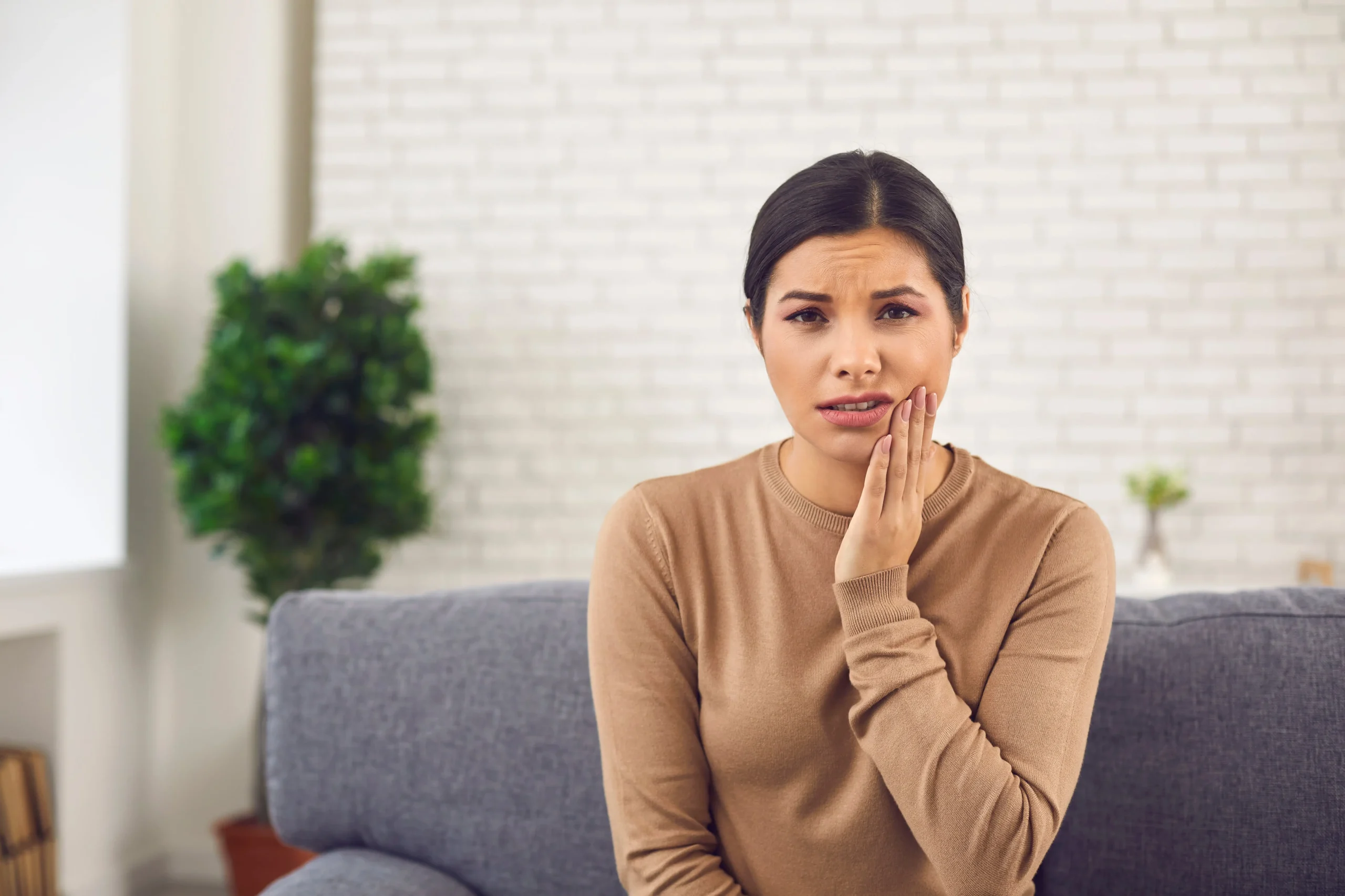 A woman seated on a couch holding her hand to her cheek wincing in pain