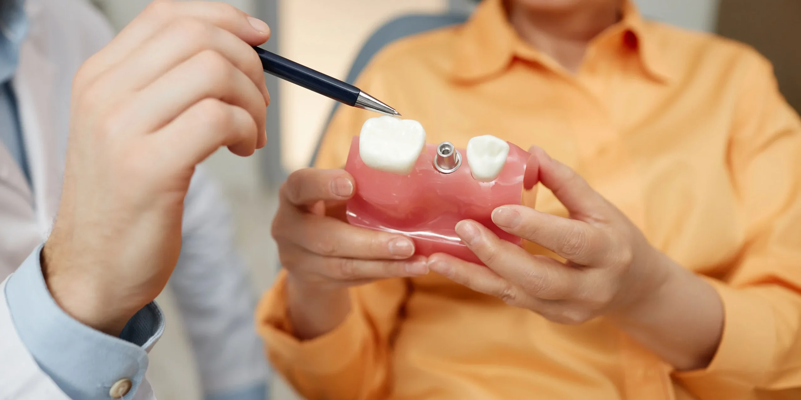 Implant abutments A person holding a dental tooth model while a dentist points at a tooth
