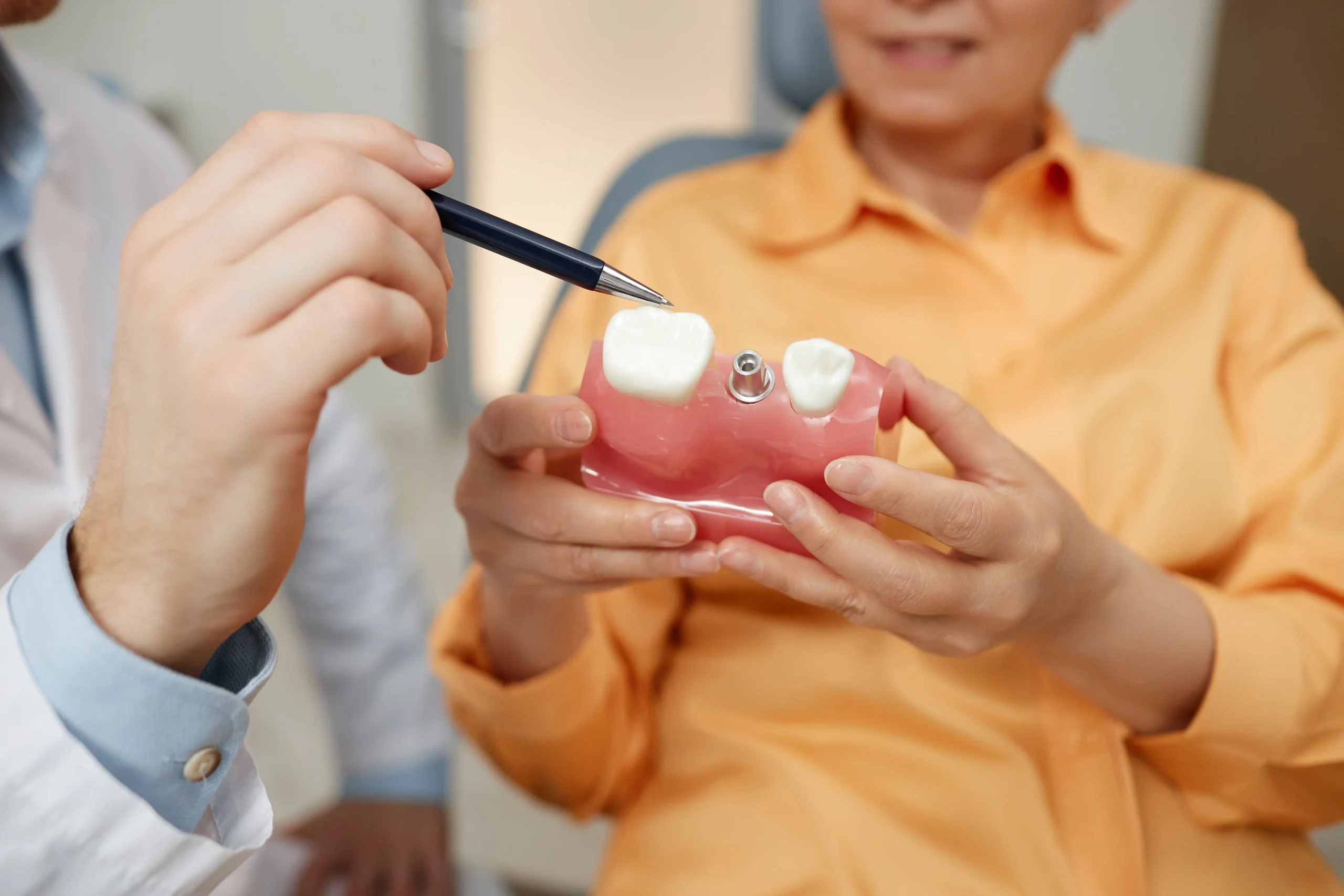 A person holding a dental tooth model while a dentist points at a tooth