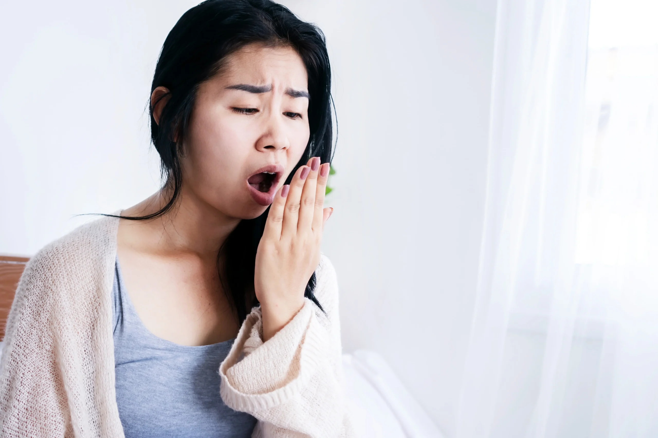 A woman holding her hand to her mouth trying to smell her breath
