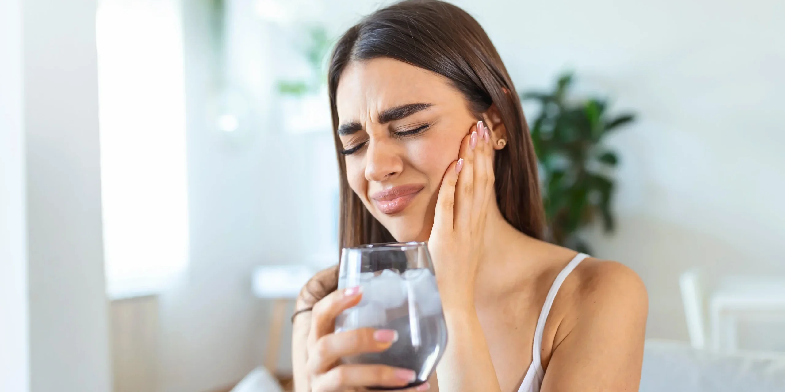 Woman wincing in pain A woman drinking a cold glass of water and wincing in pain while holding her cheek.