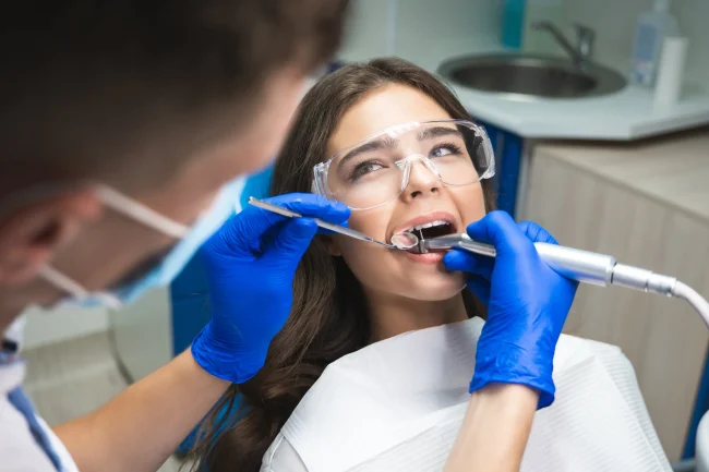 A young woman on a dental chair wearing protective eye gear while a dentist performs a treatment
