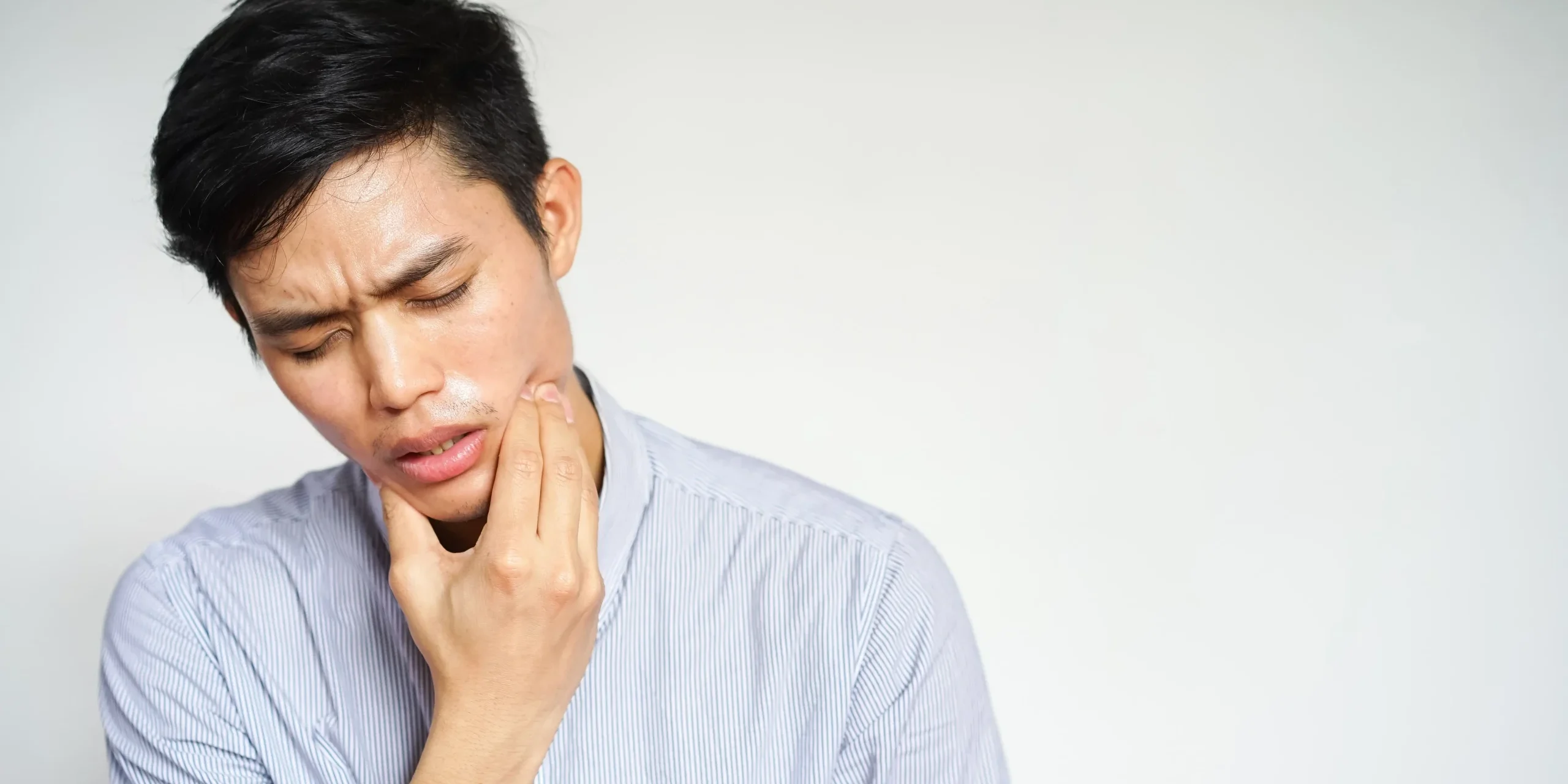 A man wincing in pain while holding his hand to his cheek