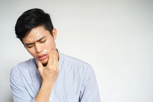 A man wincing in pain while holding his hand to his cheek
