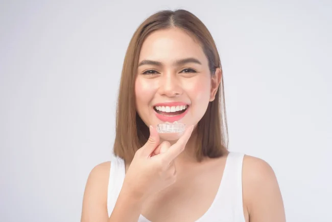 A woman holding clear aligners while smiling