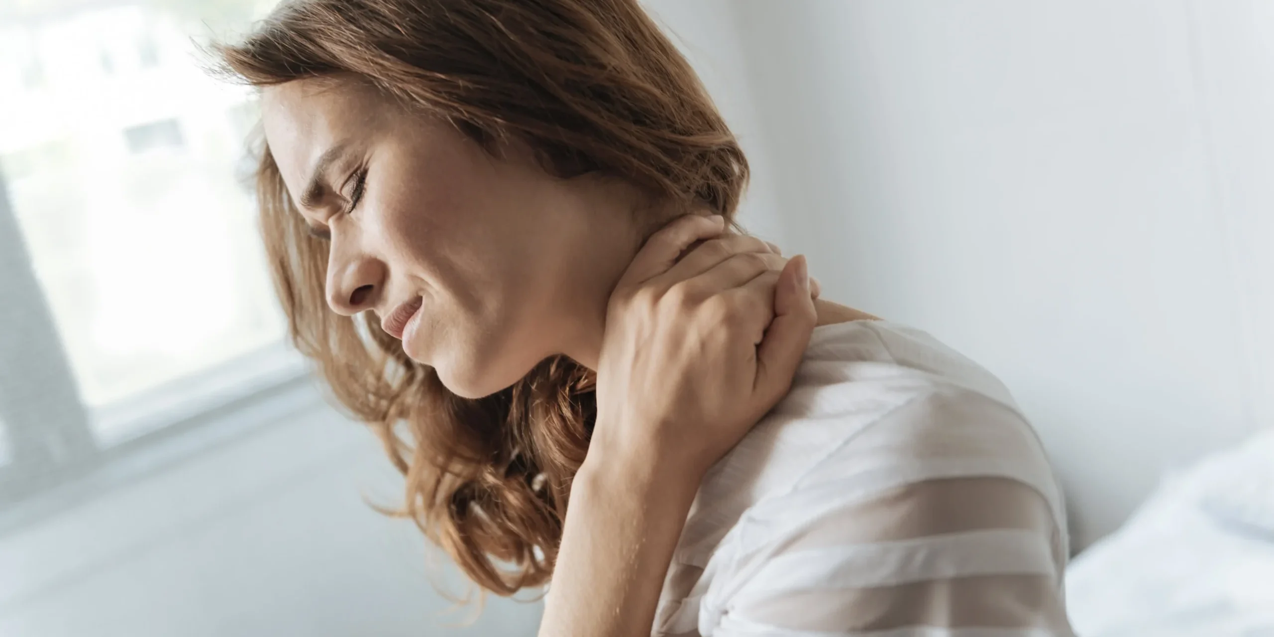 A woman wincing in pain while holding her neck
