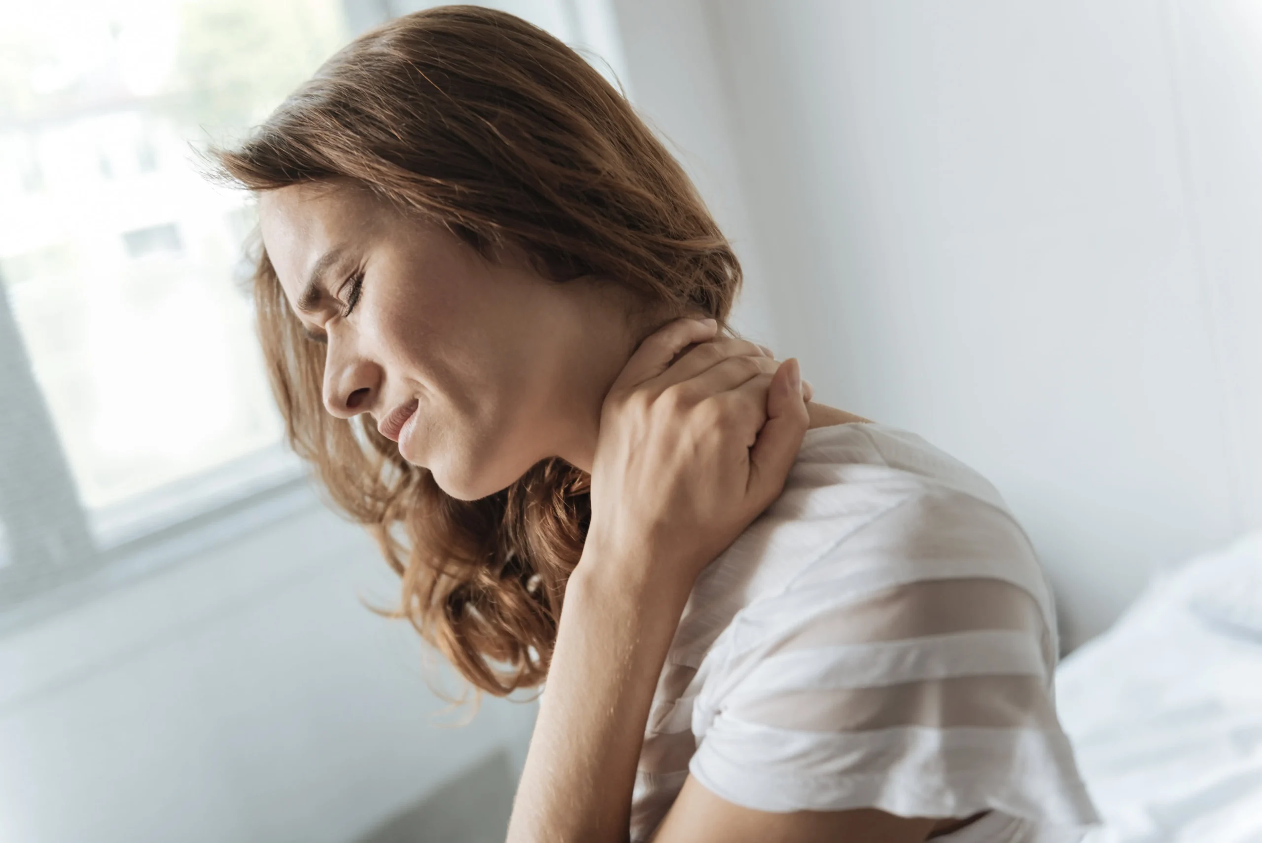 A woman wincing in pain while holding her neck