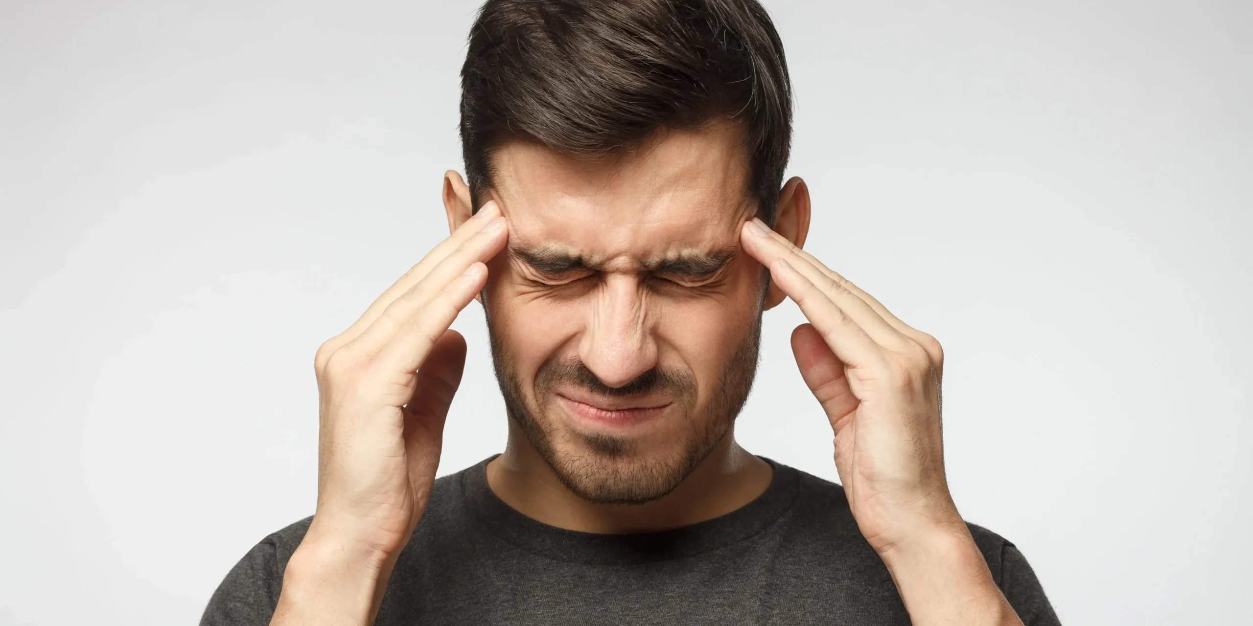 A man holding his hands to his head wincing in pain with a headache