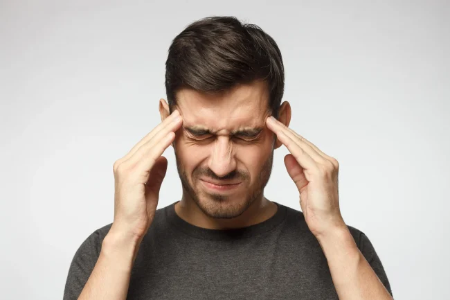A man holding his hands to his head wincing in pain with a headache