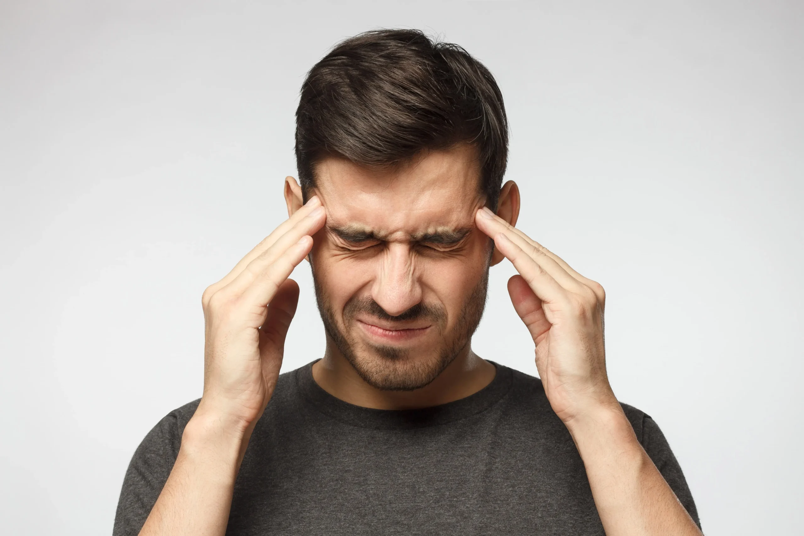 A man holding his hands to his head wincing in pain with a headache