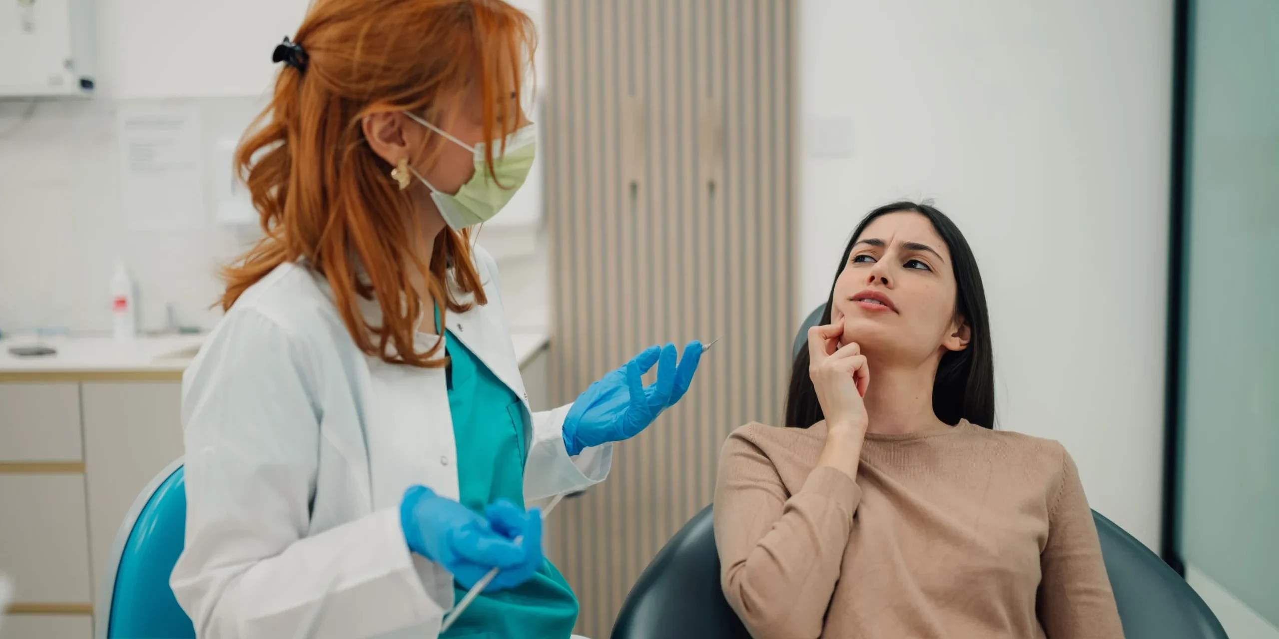 A dentist at a consultation with a female patient that seems to have a tooth ache