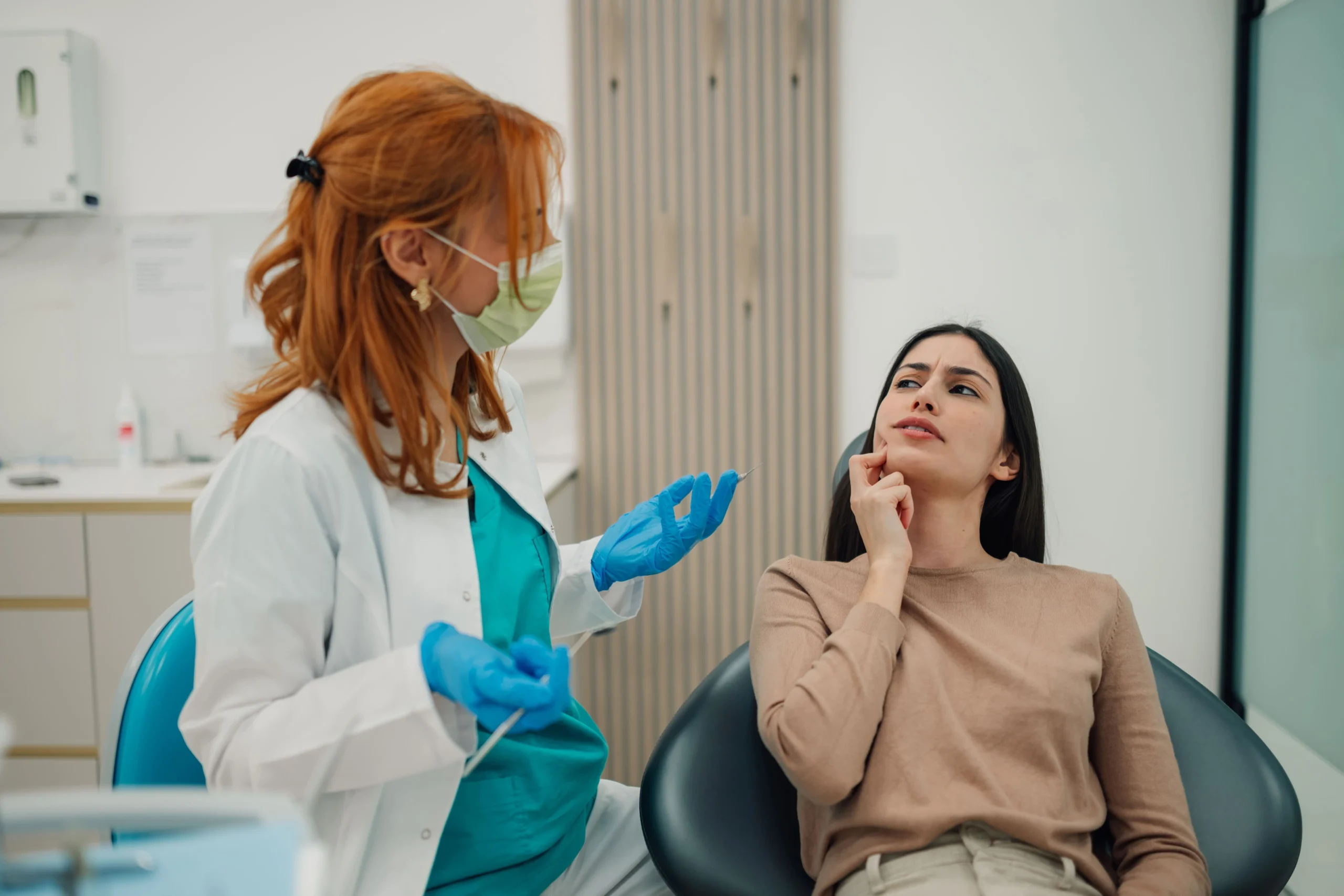 A dentist at a consultation with a female patient that seems to have a tooth ache