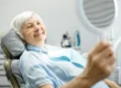 Elderly lady looks at her new teeth in the mirror at the dentist