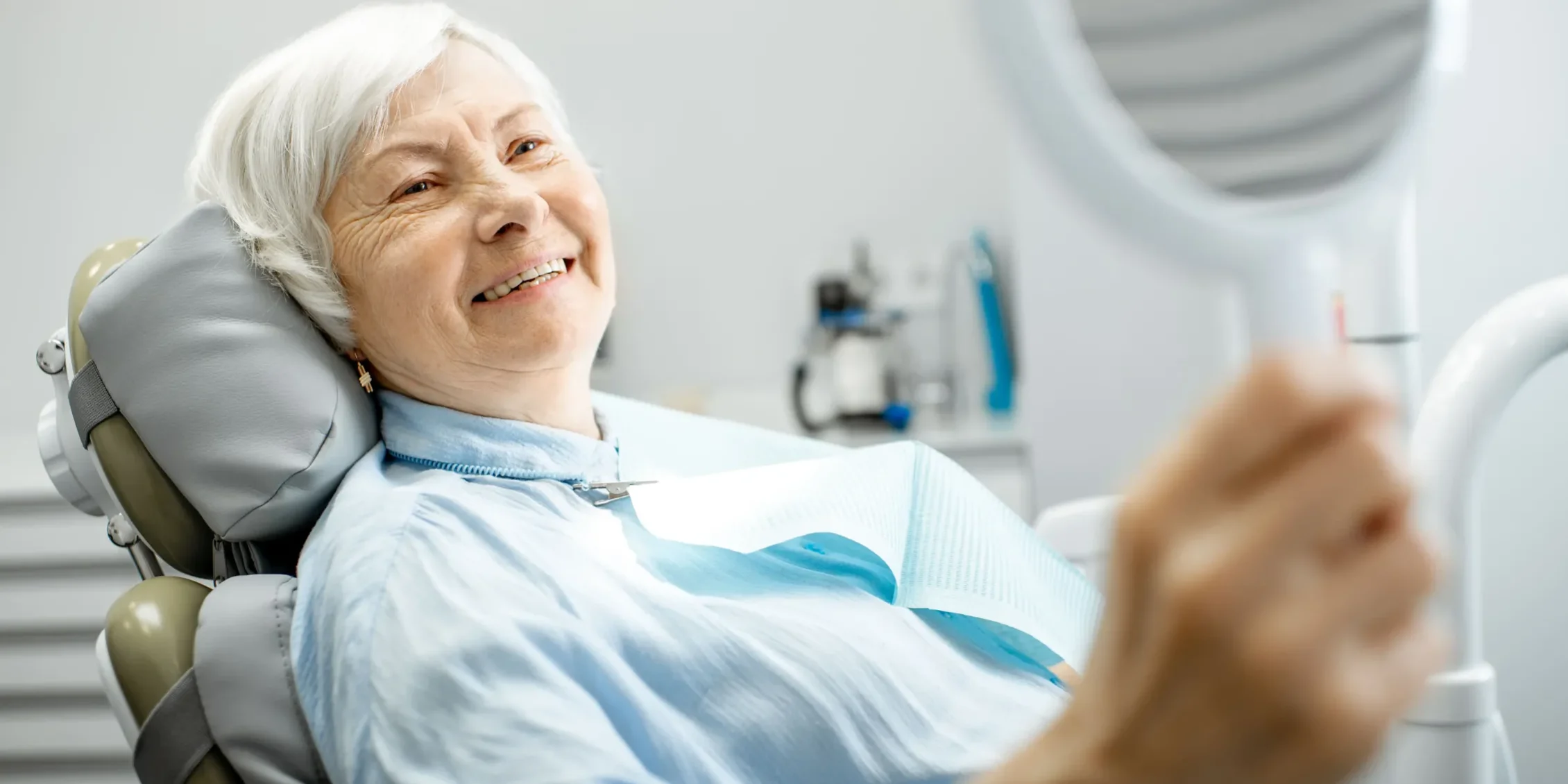 Elderly lady looks at her new teeth in the mirror at the dentist