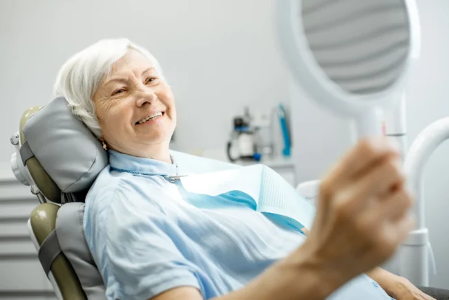 Elderly lady looks at her new teeth in the mirror at the dentist